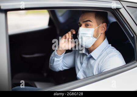 Nahaufnahme eines arabischen Geschäftsmannes in einer Gesichtsmaske, die im Auto sitzt Stockfoto