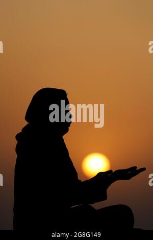 Silhouette einer muslimischen Frau in Abaya, die bei Sonnenuntergang mit ihren Händen betet, Vereinigte Arabische Emirate, Naher Osten Stockfoto