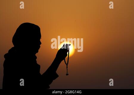 Silhouette einer muslimischen Frau, die Gebetsperlen in ihren Händen hält und bei Sonnenuntergang betet, Vereinigte Arabische Emirate, Naher Osten Stockfoto