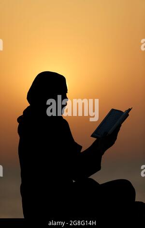 Silhouette einer muslimischen Frau, die bei Sonnenuntergang den Edlen Koran liest, Vereinigte Arabische Emirate, Naher Osten Stockfoto