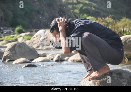 Ein gut aussehender bärtiger und langhaariger junger Mann, der sein Gesicht im Fluss wäscht Stockfoto