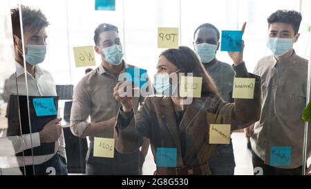 Geschäftsleute, die Einwegmasken tragen, Brainstorming mit Post-it-Notizen an der Wand Stockfoto