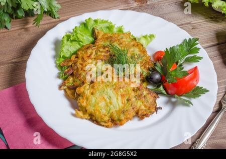 Gemüsezucchini-Pfannkuchen mit Kräutern auf einem weißen Teller aus nächster Nähe Stockfoto