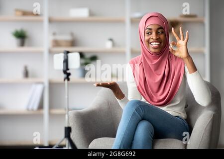 Fröhliche Schwarze Muslimische Bloggerin In Hijab, Die Video-Rezension An Der Kamera Einfängt Stockfoto