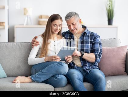 Reifes Paar mit Tablet, das zu Hause auf der Couch sitzt, im Internet surft, online chattet, im Webshop einkauft Stockfoto