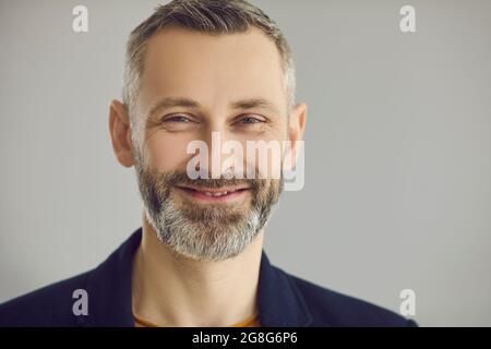 Porträt eines glücklichen bärtigen, reifen Mannes, der auf grauem Studiohintergrund vor der Kamera lächelt Stockfoto