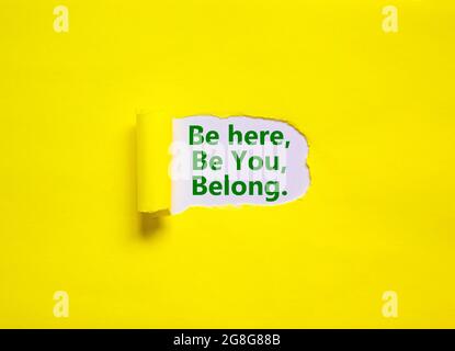 Sie gehören hier Symbol. Hinter zerrissenem gelbem Papier erscheinen Worte: „sei hier, sei du, gehöre“. Gelber Hintergrund. Unternehmen, Vielfalt, Inklusion, Belongi Stockfoto