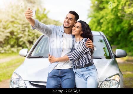 Liebevolles gemischtes Rennpaar mit dem Auto stehend, Selfie macht Stockfoto