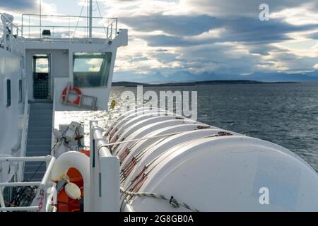 Großer weißer Tank, der an einem Boot befestigt ist, das durch die Lofoten Inseln im Meer segelt. Dramatische Wolken und Gebirgskette am fernen Horizont. Stockfoto