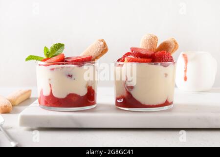 Sommerdessert in mehreren Lagen in Gläsern mit Plätzchen Savoyardi, Mascarpone und mit Schlagsahne verzierten Erdbeeren. Nahaufnahme. Italienische Tiramisu mit Summe Stockfoto