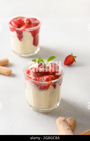 Sommerdessert in mehreren Lagen in Gläsern mit Plätzchen Savoyardi, Mascarpone und mit Schlagsahne verzierten Erdbeeren. Nahaufnahme. Italienische Tiramisu mit Summe Stockfoto