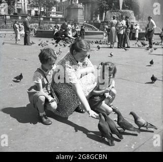 In den 1950er Jahren, mit ihren zwei jungen Töchtern neben ihr, fütterte eine Dame die Tauben am Trafalgar Square, London, England, Großbritannien. Eine traditionelle Aktivität seit mehr als hundert Jahren, wurden Schwärme von Tauben auf den Platz herabsteigen, um Nahrung von denen zu erhalten, die das berühmte Wahrzeichen von Central London besuchen. Stockfoto