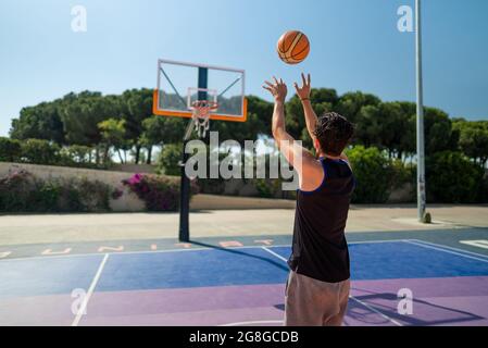 Rückansicht des männlichen Sportlers, der Basketball spielt und den Ball auf dem Spielplatz wirft, Blick von hinten. Präzisionsschuss Stockfoto