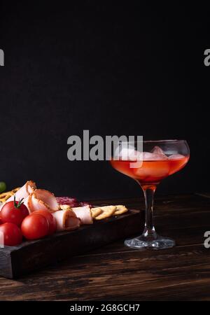 Glas mit rotem Likör und Wurstkarton, alkoholischer Cocktail mit Vorspeise, Nahaufnahme. Stockfoto