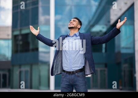 Emotionaler arabischer Mann in formellem Anzug, der die Hände hochhebt Stockfoto