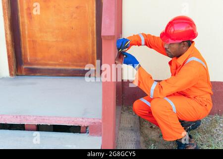 Afrikanischer Arbeiter in Overalls . Afrikanischer Mann, der außerhalb des Hauses Messungen annahm Stockfoto