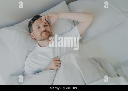 Junger, müder bärtiger Mann, der mit offenen Augen auf dem Bett liegt Stockfoto