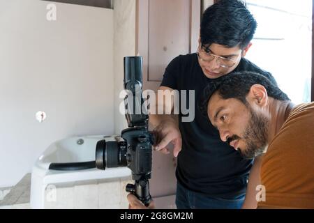 Blick auf zwei hispanische Männer, die die Kamera auf dem Stativ im Studio aufsetzen Stockfoto