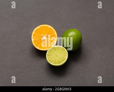 Limette und orangefarbene Zitrone auf grauem Hintergrund. In Scheiben geschnittene und ganze Zitrusfrüchte auf einem Steintisch. Draufsicht, flach liegend. Stockfoto