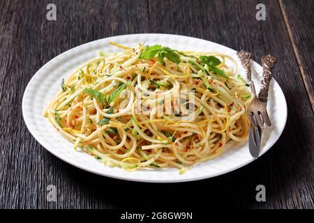 Sommer-Spaghetti alla carrettiera mit Minzblättern, Zitronenschale, Pecorino-Käse, Chilischoten-Flocken, Petersilie und geriebenen Zucchini auf einem weißen Teller Stockfoto