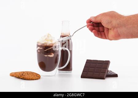 Männliche Hand mit Löffel über Tasse Schokoladenmilchshake und Schlagsahne: Schokoladenkonzept. Stockfoto