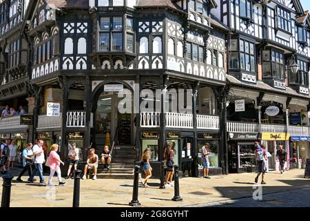 Chester, England - Juli 2021: Menschen, die an der schwarz-weißen Architektur der Gebäude in den Reihen im Stadtzentrum vorbeigehen. Stockfoto