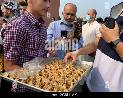 Männer, die arabische Süßigkeiten als Menschenmenge genießen muslimische Gläubige versammeln sich im Freien an der Hamilton Mountain Moschee, um das Eid-Fest anzubeten und zu feiern. Stockfoto