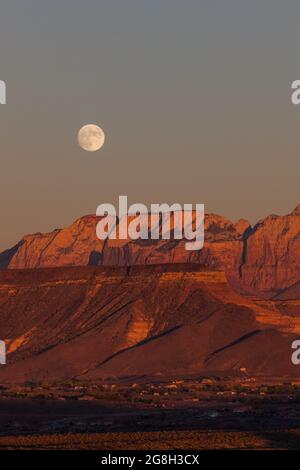 Der Vollmond, der über den dramatischen Bergen des Zion National Park aufgeht und von der untergehenden Sonne mit klarem Himmel erleuchtet wird. Stockfoto