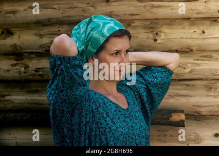 Das Porträt einer Frau in traditionellem Bauernkleid bindet ein Kopftuch vor dem Hintergrund einer Blockwand Stockfoto