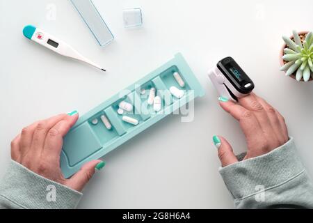 Patientenhände mit Pillen und Pulsoximeter, digitales Fingergerät zur Messung der Sauerstoffsättigung in der Lunge. Reife kaukasische weibliche Hand. Reduziert Stockfoto