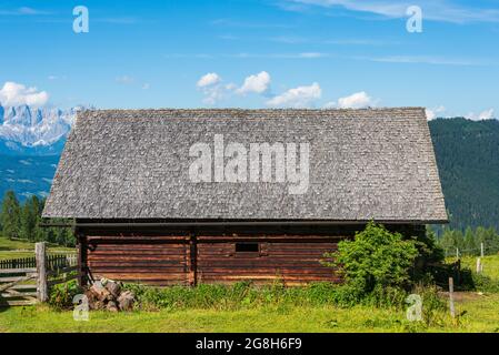 Ein alpiner Holzschuppen vor dem Hintergrund hochalpiner Berge. Verschwommene, verwitterte Holzschindeln, verblasst von Sonne, Regen und Schnee. Holzstruktur Stockfoto