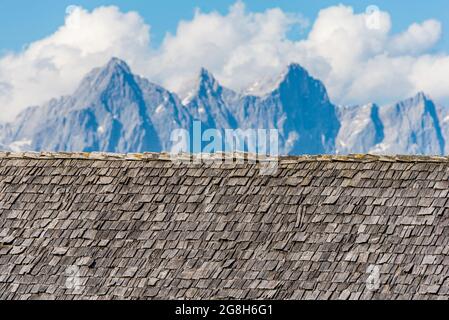 Verwittert und verblasst von der Sonne, Regen und Schnee Holzschindeln, die das Dach eines alpinen Hauses vor dem Hintergrund der hochalpinen Berge sind. Wo Stockfoto