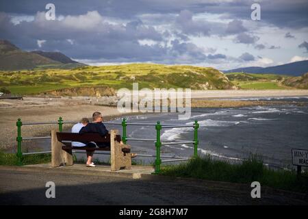 Ein Paar sitzt auf einer Bank und betrachtet die Küstenlinie von Nord-Wales in der Stadt Criccieth, Wales - vereinigtes Königreich. Stockfoto