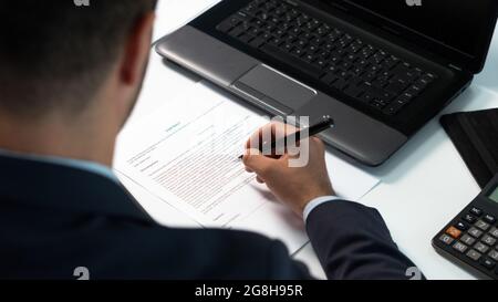 Ein Geschäftsmann schaut sich die Vertragsbedingungen an, bevor er ein Zeichen auf Papier setzt. Mann, der eine rechtliche Vereinbarung, Vertrag unterzeichnet. Rückansicht. Stockfoto
