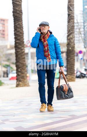 Bärtiger Großvater mit einer Handtasche geht auf der Straße, während er ruft Stockfoto