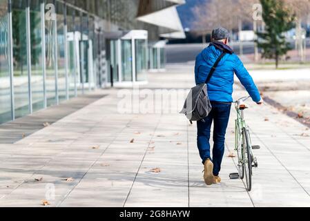 Älterer Mann, der mit dem Fahrrad auf der Stadtstraße mit einer Handtasche unterwegs ist Stockfoto