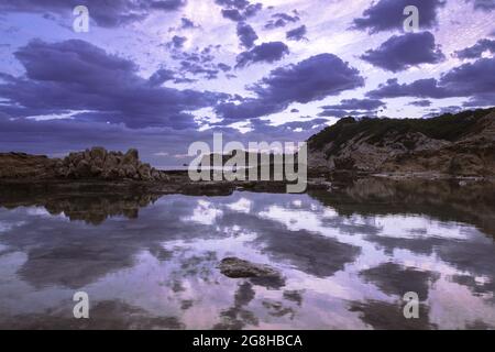 Wunderschöne Aufnahme von großen Klippen, die sich nach dem Sonnenuntergang im ruhigen türkisfarbenen Meer spiegeln Stockfoto