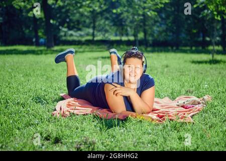 Frau hört im Sommer Musik, während sie sich im öffentlichen Park ausruhen. Stockfoto