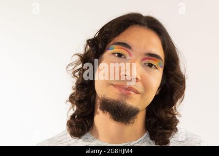 Porträt eines schwulen Mannes in Make-up mit einem Regenbogen in den Augen auf einem weißen Hintergrund lächelnd Stockfoto