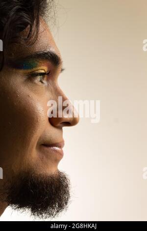 Porträt eines schwulen Mannes in Make-up mit einem Regenbogen in den Augen auf einem weißen Hintergrund lächelnd Stockfoto
