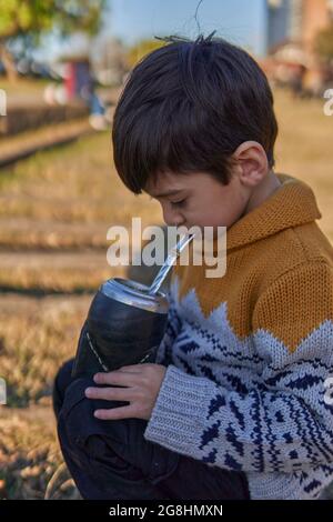 Portrait eines brünetten Kindes im Park, das Yerba Mate an den Eisenbahnschienen trinkt. Argentinischer Brauch, vertikal Stockfoto