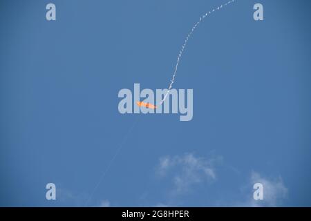 Ein selbstgemachter, roter Drachen mit weißer Schnur und Schwanz fliegt an einem Sommertag in einem blauen Himmel mit ein paar weißen Wolken. Stockfoto