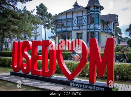 Zinnowitz, Deutschland. Juli 2021. Urlauber und Tagesbesucher sind auf der Strandpromenade hinter dem Schild „Usedom“ unterwegs. Hotels, Pensionen und Campingplätze in Mecklenburg-Vorpommern sind in den kommenden Wochen gut ausgebucht. Nach Angaben des Tourismusverbandes könnte sich die Saison wie im vergangenen Jahr bis in den September erstrecken. Quelle: Jens Büttner/dpa-Zentralbild/dpa/Alamy Live News Stockfoto