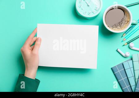 Weibliche Hand mit leerem Blatt Papier, Papeterie, Tasse Kaffee und Wecker auf farbigem Hintergrund Stockfoto