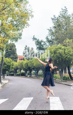 Vertikale Aufnahme einer lateinischen Balletttänzerin, die anmutig auf Zehenspitzen auf einem Fußgängerweg in schwarzem Outfit und spitzenschuhen läuft Stockfoto