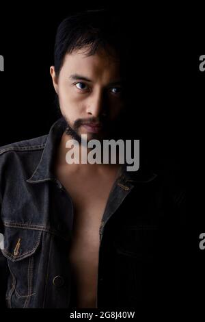 Ein Mann, der ein Jeanshemd, ein wildes Gesicht, einen Bart trägt.Studioaufnahme, schwarze Szene, Nahaufnahme, Kopf und Gesicht Stockfoto