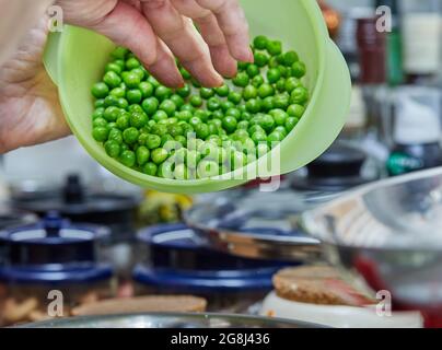 Der Koch stellt grüne Erbsen in eine Schüssel, um Backwaren mit Spargel und Erbsen zu machen. Schritt für Schritt Rezept Stockfoto