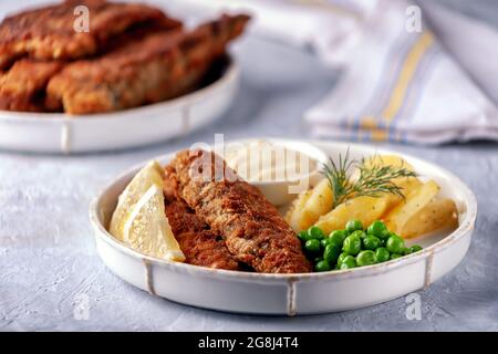 Gebratener Fisch mit grünen Erbsen, Zitrone und gebratenen Kartoffeln Stockfoto