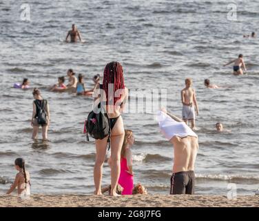 Junge Frau im Bikini steht am Strand am finnischen Golf mit schwimmenden Menschen, St. Petersburg, Russland Stockfoto