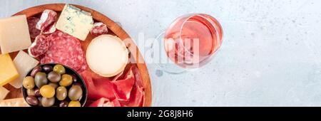 Panorama-Banner mit Aufschnitt und Käse, von oben mit einem Glas Rosenwein aufgenommen. Prosciutto di Parma Schinken, Blauschimmelkäse, Oliven und Cracker, Gourmet-Antipasti Stockfoto